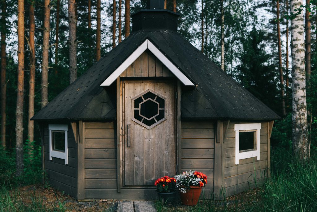 Our cottage via Mokkiavain Cottages. A small log cabin in the middle of the woods in Tampere. Has a small chimney and white windows.