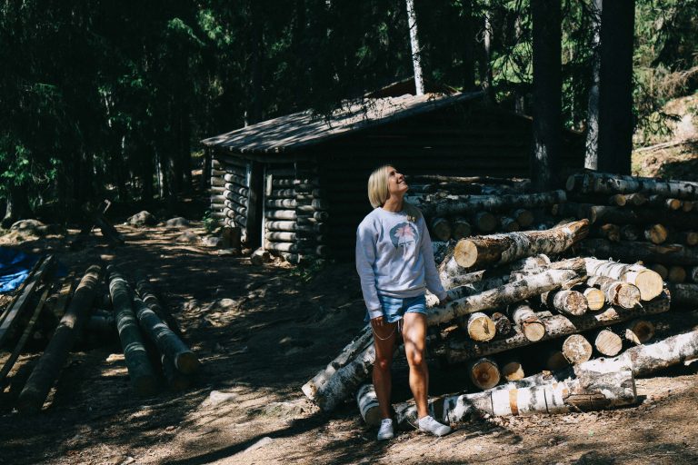A girl stood in a forest in Tampere, surrounded by chopped woods and a small log cabin.