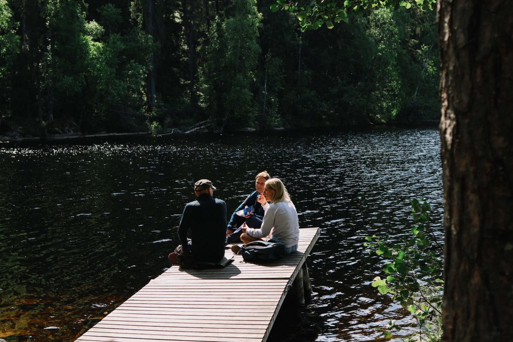 Helvetinjärvi National Park. A group of three hikers have lunch on a jetty overlooking a lake in Helvetinjärvi National Park.